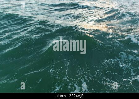 Surface d'eau de mer sombre bleu-vert avec morceaux de mousse et reflets, motif vagues, texture photo d'arrière-plan Banque D'Images
