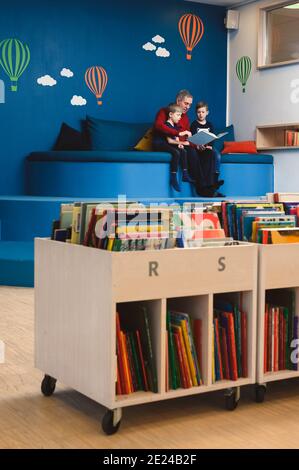 Grand-père lisant le livre aux petits-fils dans la bibliothèque Banque D'Images