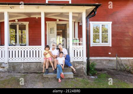 Parents avec deux filles assises devant la maison Banque D'Images