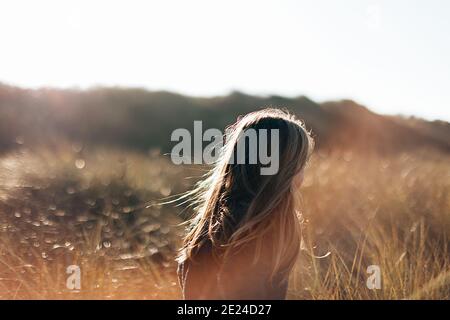 vue arrière d'une jeune fille avec des cheveux longs courant dans un pré au coucher du soleil Banque D'Images