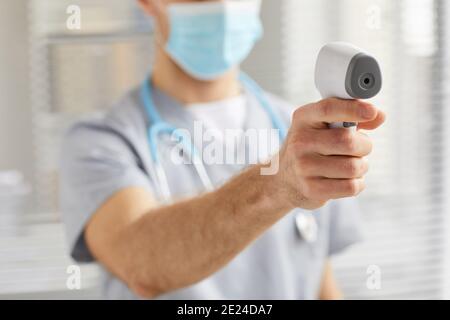Gros plan d'un médecin masculin méconnaissable pointant le thermomètre infrarouge vers la caméra tout en vérifiant la température dans la clinique, copier l'espace Banque D'Images