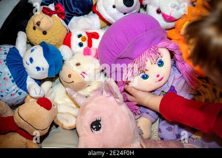 différents types de jouets souples en peluche sur le sol partout dans la chambre d'un enfant avec un tourbillon jouant avec elle poupée préférée Banque D'Images