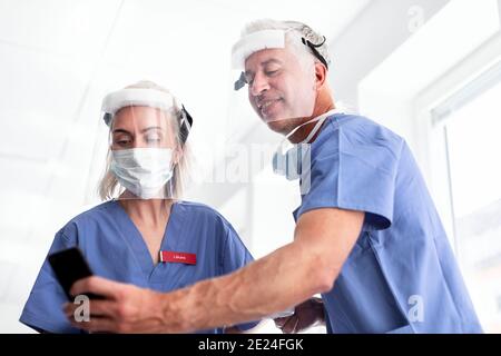 Les médecins portant un équipement de protection individuelle regardant le téléphone Banque D'Images