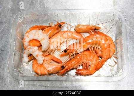 Crevettes fraîches entières cuites dans un récipient en plastique avec deux queues décortiquées dans un concept de gourmet ingrédients de fruits de mer pour la cuisine ou un Banque D'Images