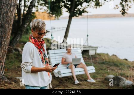 Femme heureuse utilisant un téléphone cellulaire, homme sur un banc oscillant sur fond Banque D'Images