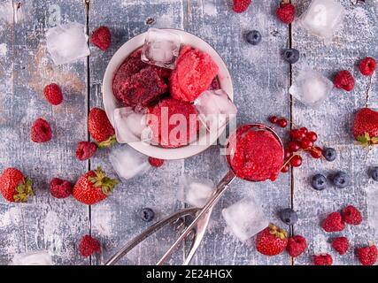 Boules de fraise maison, de cassis rouge, de framboise, de crème glacée aux bleuets, sorbet dans un bol, de pelles, de baies et de glaçons sur le backgroun bleu en bois Banque D'Images