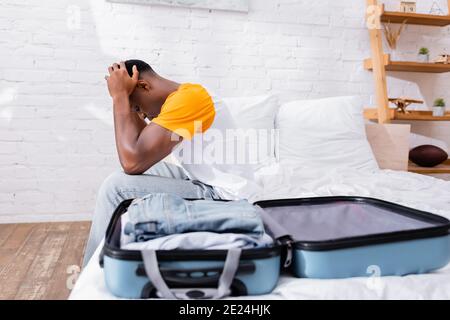 Triste africain américain assis près d'une valise sur un premier plan flou sur le lit Banque D'Images