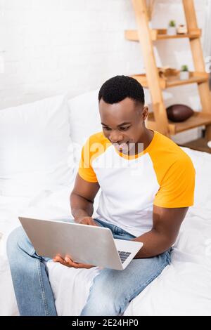 Joyeux travailleur indépendant afro-américain utilisant un ordinateur portable au lit le matin Banque D'Images