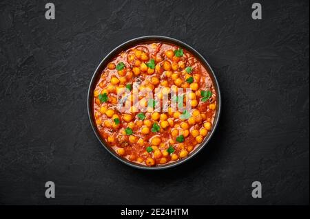 Chana Masala ou Chole dans un bol noir sur table en ardoise sombre. Cuisine indienne, légumes, pois chiches, plat de curry. Plats et repas végétariens épicés asiatiques. Vue de dessus Banque D'Images