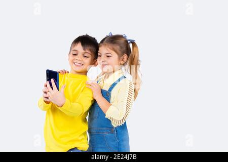 Des enfants d'âge préscolaire heureux avec des appels vidéo sur smartphone et souriant sur fond blanc. Banque D'Images