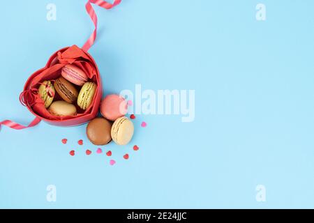 Boîte rouge en forme de coeur ouvert plein de macarons sur fond bleu. Décoration de Saint-Valentin, anniversaire, fête des mères et carte d'anniversaire. Banque D'Images