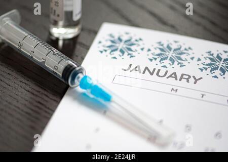 Gros plan d'une seringue médicale placée sur un calendrier de janvier avec un flacon de vaccin en arrière-plan, symbolisant la vaccination programmée Banque D'Images