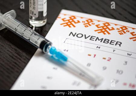 Gros plan d’une seringue médicale placée sur un calendrier de novembre avec un flacon de vaccin en arrière-plan, symbolisant la vaccination programmée Banque D'Images