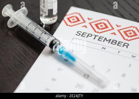 Gros plan d’une seringue médicale placée sur un calendrier de septembre avec un flacon de vaccin en arrière-plan, symbolisant la vaccination programmée Banque D'Images