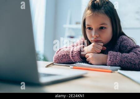 Une jeune fille contrariée regarde un ordinateur portable au bureau sur un premier plan flou Banque D'Images