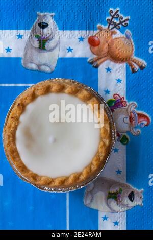 Tarte aux pommes de terre hachée glacée de Sainsburys sur une serviette de Noël festive - pâtisseries fourrées de viande hachée, recouvertes de glaçage blanc doux Banque D'Images