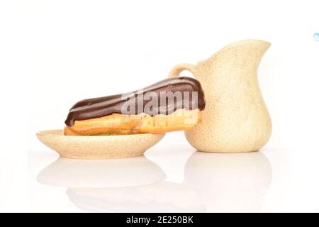 Un chocolat eclair sur une soucoupe en céramique avec un pot à lait en céramique, gros plan, isolé sur du blanc. Banque D'Images