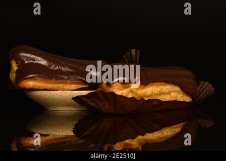 Deux eclairs au chocolat avec une soucoupe en céramique sur fond noir. Banque D'Images