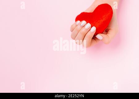 Une main femelle tendre tient un coeur rouge doux sur un fond rose avec espace publicitaire vide. Banque D'Images