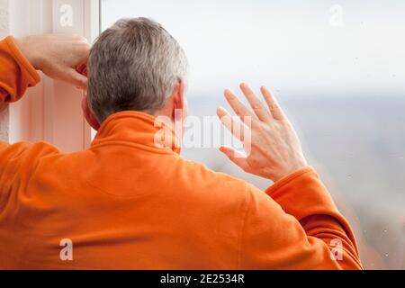 Homme mature à la maison en raison de la quarantaine Covid-19 regardant dehors de fenêtre avec gouttes de pluie - focus sur la main Banque D'Images