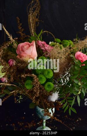 Floristry, un beau bouquet féminin naturel orné de roses, d'œillets, de graminées et de brindilles vertes sur fond noir. Banque D'Images