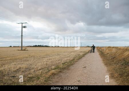 Paysage de champ sec et fauchée avec un jeune homme marchant à côté de tu son vélo Banque D'Images