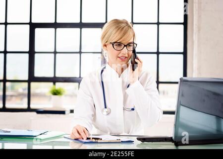 Prise de vue d'une femme médecin effectuant un appel et utilisant un ordinateur portable tout en travaillant dans le bureau du médecin. Banque D'Images