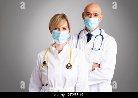 Prise de vue de médecins féminins et masculins portant des masques et se tenant ensemble sur un fond gris isolé. Équipe médicale. Médecins portant des masques pour le pré Banque D'Images