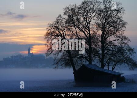 L'abbaye d'Andechs (Kloster Andechs) dans le brouillard au coucher du soleil, avec une grange et des arbres au premier plan Banque D'Images