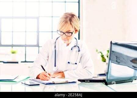 Portrat photo d'une femme médecin assise au bureau et écrivant quelque chose pendant qu'elle travaille dans le bureau du médecin. Banque D'Images