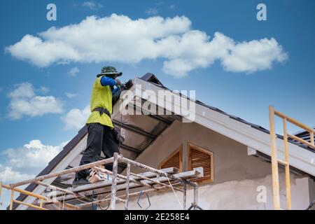 Installation par un ouvrier de la construction installer un nouveau toit en céramique, des outils de couverture, une perceuse électrique utilisée sur les nouveaux toits sur le chantier de construction. Banque D'Images