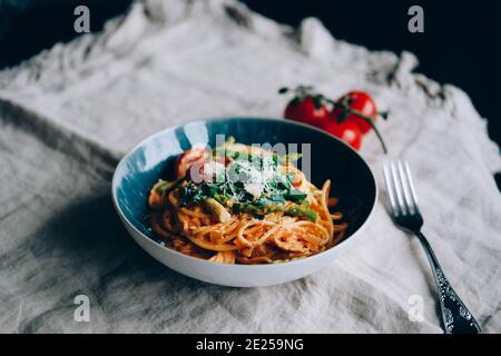 Pâtes avec asperges, sauce crémeuse à la tomate et au citron dans une assiette bleue. Banque D'Images