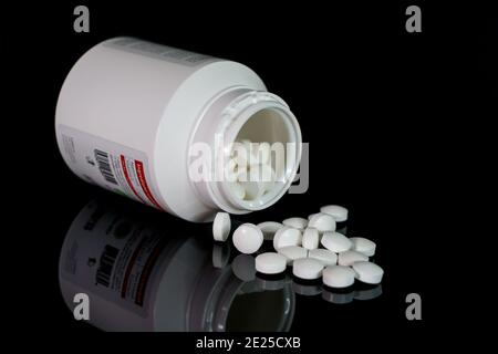 Des pilules blanches débordent d'une bouteille de pilules blanches brillantes et renversées. Banque D'Images