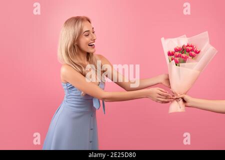Joyeuse jeune femme recevant un bouquet de belles fleurs de printemps pour Fête des femmes sur fond rose Banque D'Images