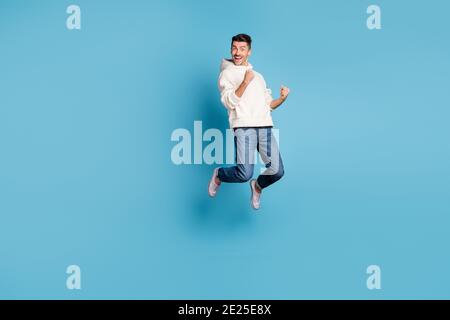 Photo pleine grandeur de jeune heureux excités fou positif homme sautant tenir les poings dans la victoire isolée sur fond bleu Banque D'Images