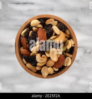 Vue de dessus d'un assortiment de noix et de fruits secs dans un bol en bois au-dessus d'un comptoir en marbre gris. Banque D'Images