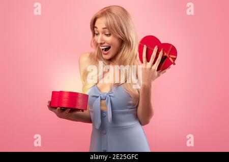 Une jeune femme se sent excitée par une boîte cadeau ouverte en forme de cœur, heureuse de recevoir la surprise de la Saint-Valentin sur fond rose Banque D'Images