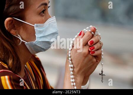 Femme portant un masque chirurgical priant avec le rosaire. Église catholique. Banque D'Images