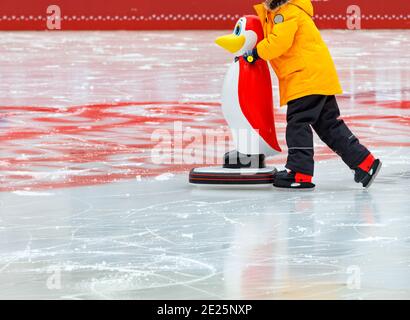 Un adolescent apprend à skate sur une patinoire en tenant un assistant, un pingouin jouet. Banque D'Images