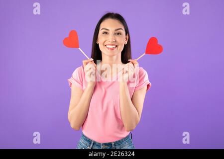 Femme souriante tenant deux coeurs et regardant l'appareil photo Banque D'Images