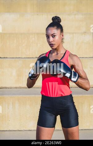 portrait vertical d'une athlète afro-américaine vêtue de noir gants de boxe et debout en position de défense Banque D'Images
