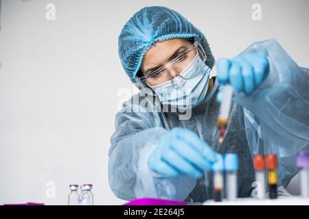 Scientifique portant des vêtements très protecteurs tenant un tube montrant positif Résultat du test Covid Banque D'Images