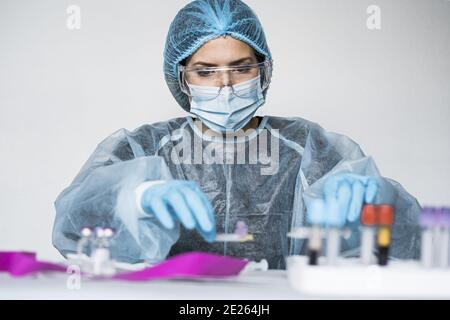 Scientifique portant des vêtements très protecteurs tenant un tube montrant positif Résultat du test Covid Banque D'Images