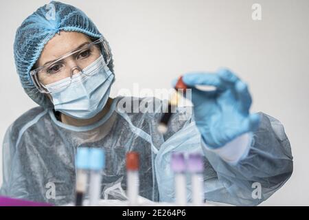 Scientifique portant des vêtements très protecteurs tenant un tube montrant positif Résultat du test Covid Banque D'Images