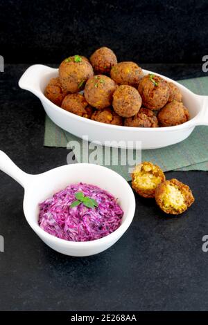 Cuisine traditionnelle du Moyen-Orient, Falafel (tamiya) avec salade de chou rouge et mayonnaise végétalienne sur fond de bois noir et nappe verte. Sélection Banque D'Images