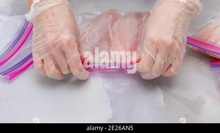 Filet de poisson frais dans des sacs à fermeture à glissière. Filet de tilapia sur fond de marbre clair, gros plan. Femme mains mettre le filet dans des sacs à fermeture à glissière pour le gel Banque D'Images