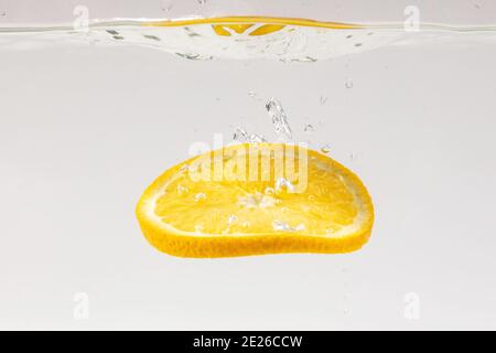 Tranche de citron flottant dans l'eau sur une surface blanche Banque D'Images