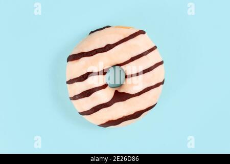 Beignet émaillé de chocolat blanc avec des rayures brunes sur la lumière arrière-plan bleu Banque D'Images