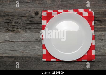 Assiette en porcelaine blanche et serviette à carreaux rouges sur une ancienne table en bois. Vue de dessus Banque D'Images