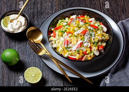 Salade de crabe de bâtonnets de surimi aux légumes : maïs, concombres, scallion, œufs, riz jasmin avec sauce lime et mayonnaise servi dans un bol noir o Banque D'Images